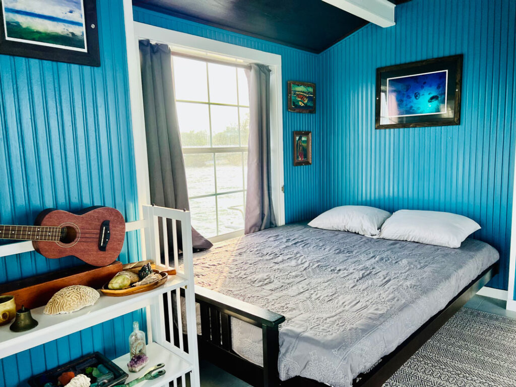 photo of the bedroom on a houseboat with blue walls, a bed and ukulele