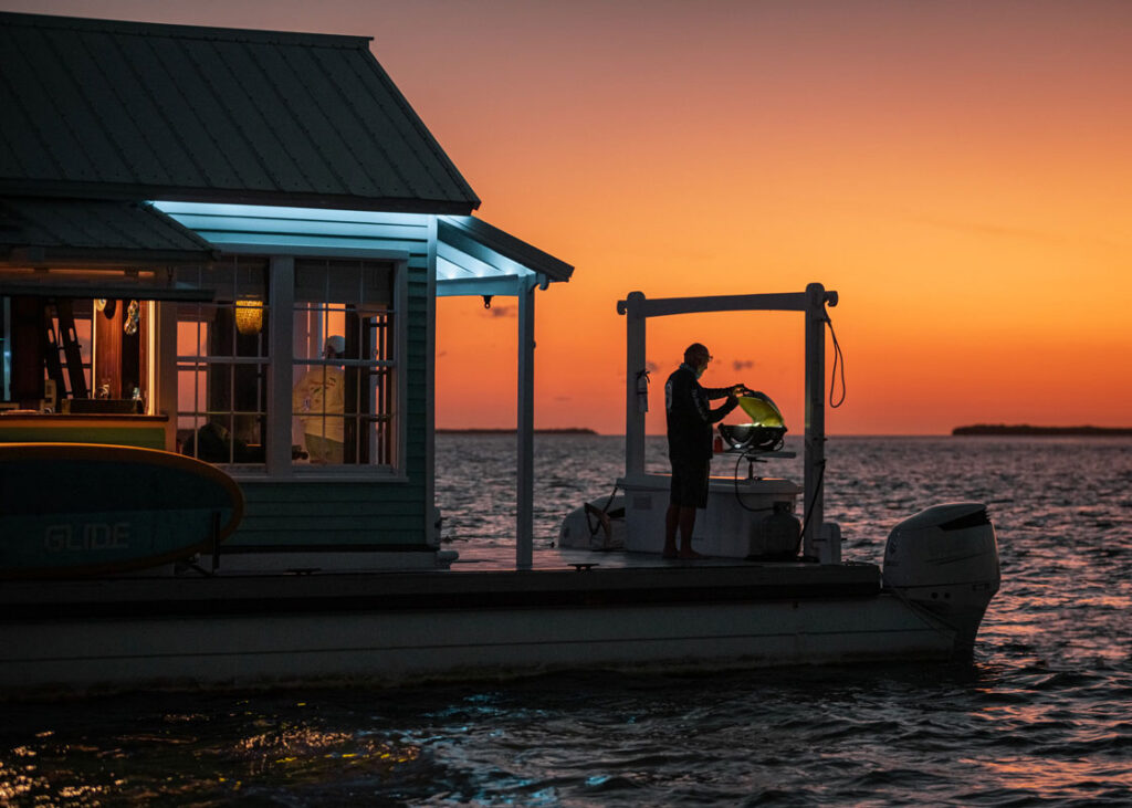 A photo of a man cooking on a houseboat at sunset.
