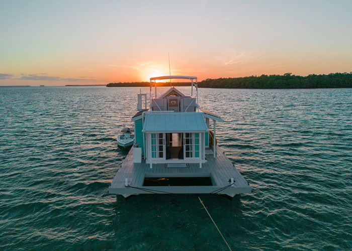 a photo of a houseboat in the water with the sunsetting behind it