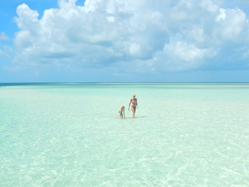 photo of a mother and daughter walking in crystal clear shallow ocean water